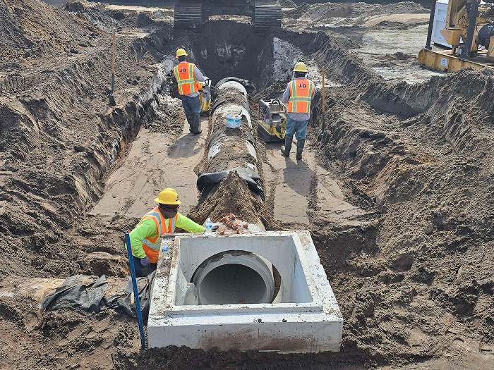 Construction site crew with equipment lay a concrete pipe line under the ground.
